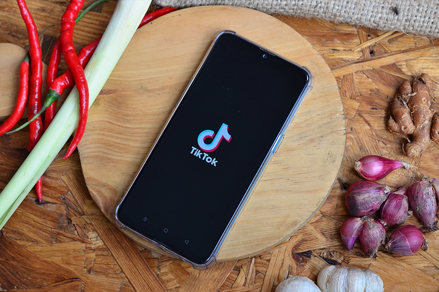  tiktok on smartphone placed on wooden board surrounded by shallots, ginger and chillies 